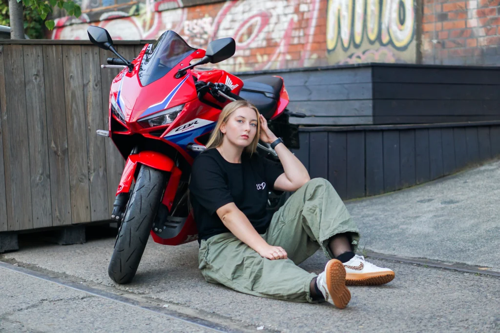 Młoda kobieta siedząca obok czerwonego motocyklu.