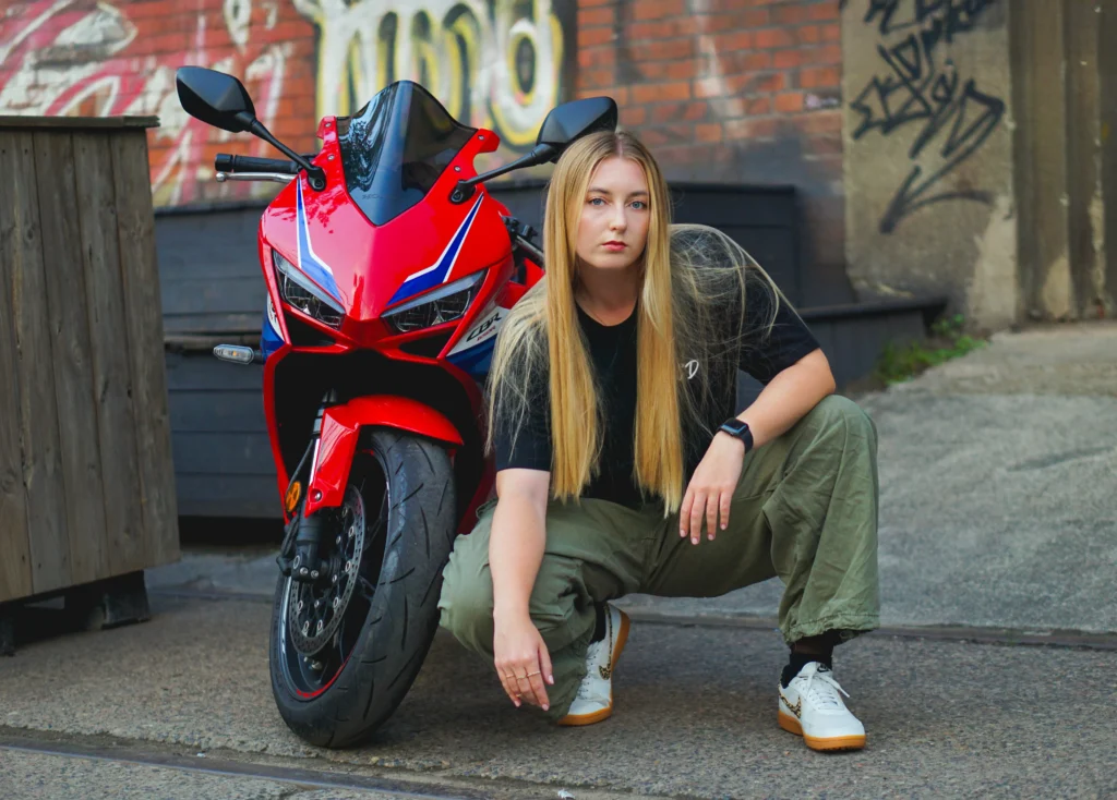 Młoda kobieta kucająca obok czerwonego motocyklu.