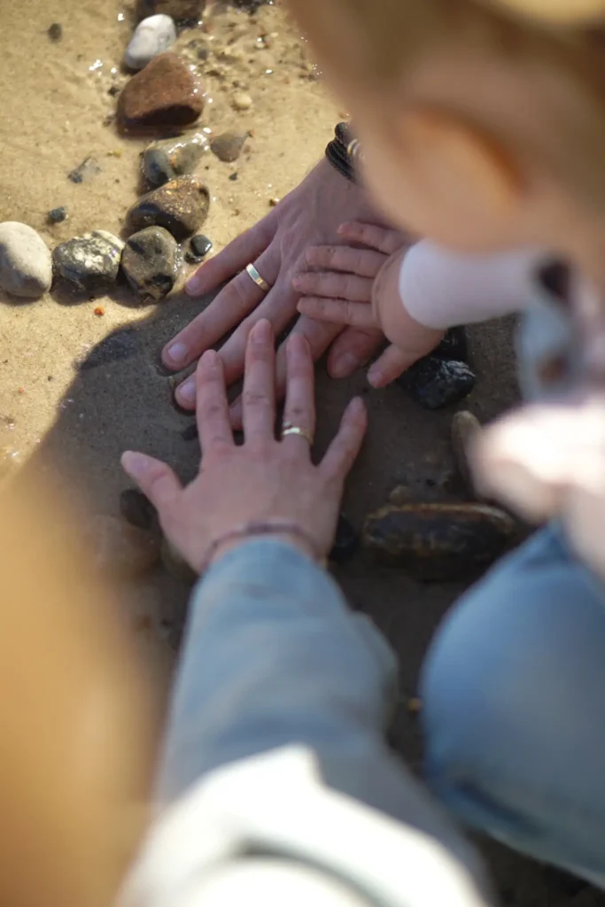 Młoda rodzina z dzieckiem na plaży przykładająca wzajemnie do siebie dłonie.