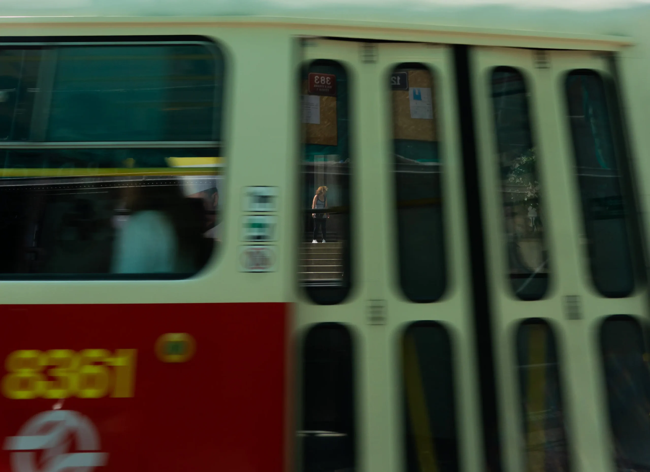 Przejeżdżający tramwaj z bliska, w odbiciu drzwi widać kobietę.